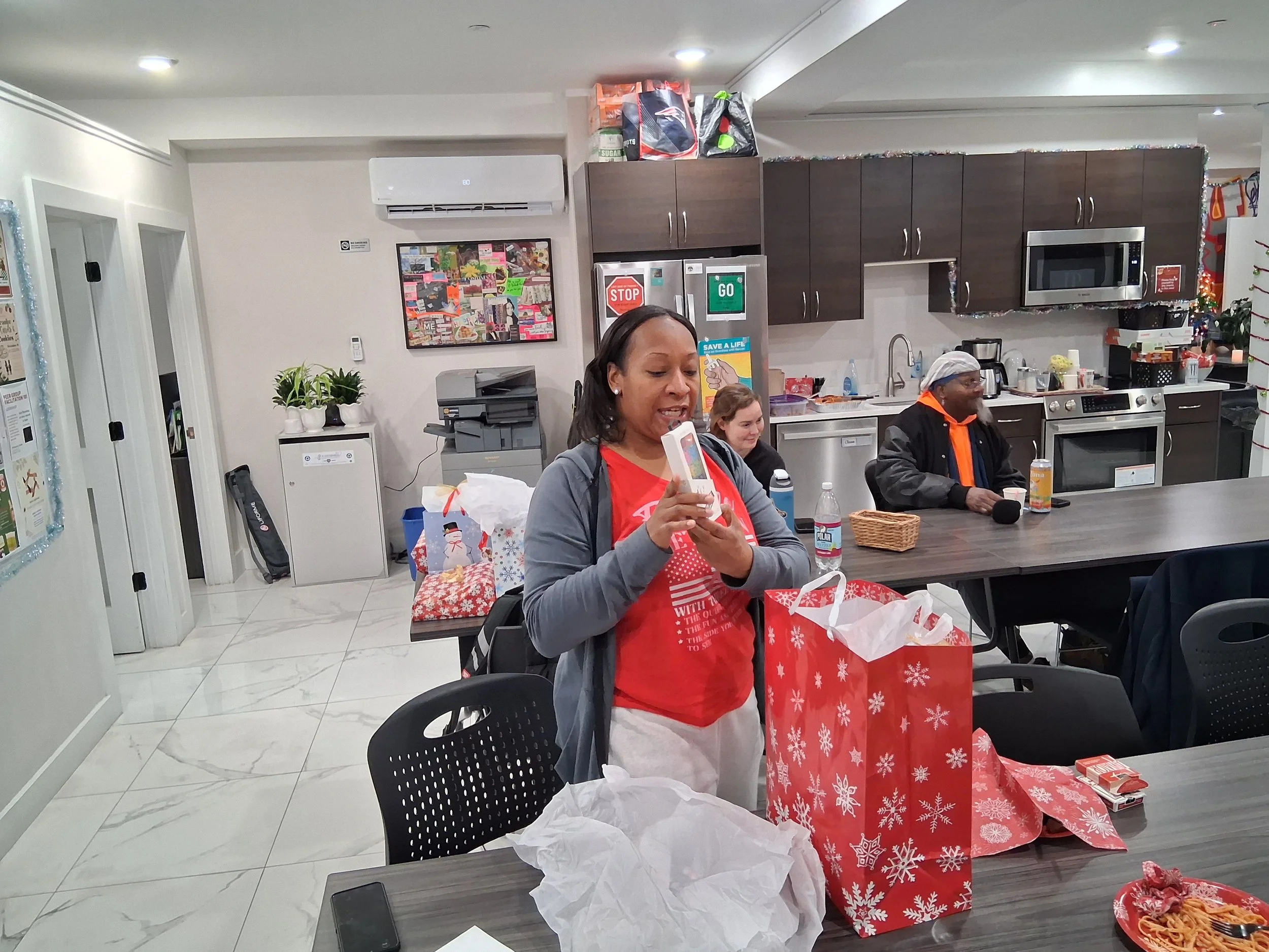 Group of people in a kitchen and dining area opening and celebrating Christmas gifts.
