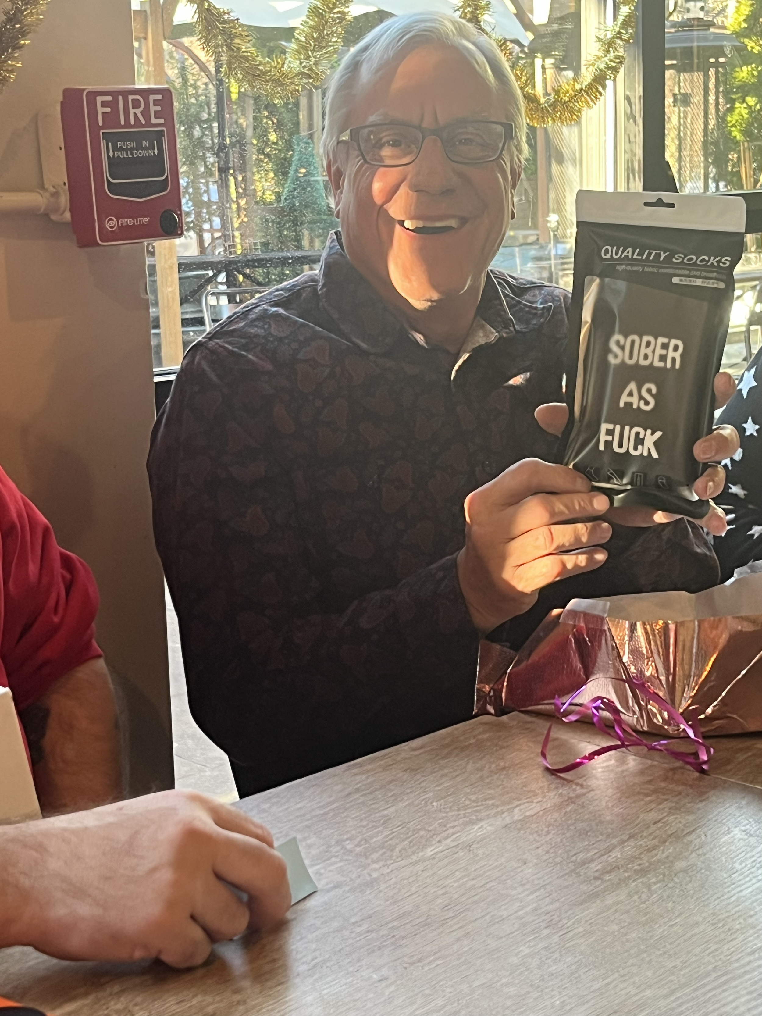 A smiling man with glasses holding a black package that has white text reading 'Sober as F**k'.