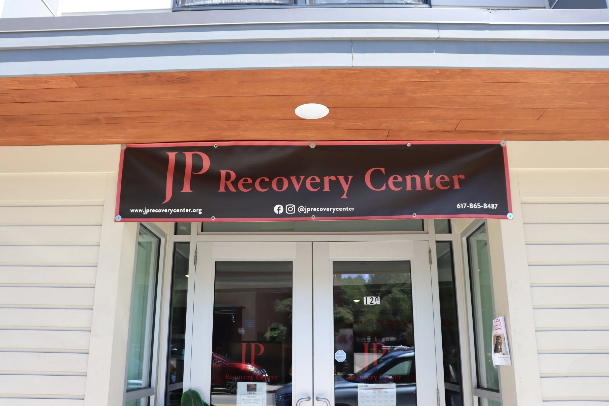 Entrance of JP Recovery Center with a black and red sign displaying the name, website, social media, and phone number.