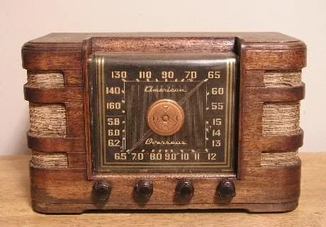 Vintage wooden radio with four control knobs and a square tuning dial in the center.