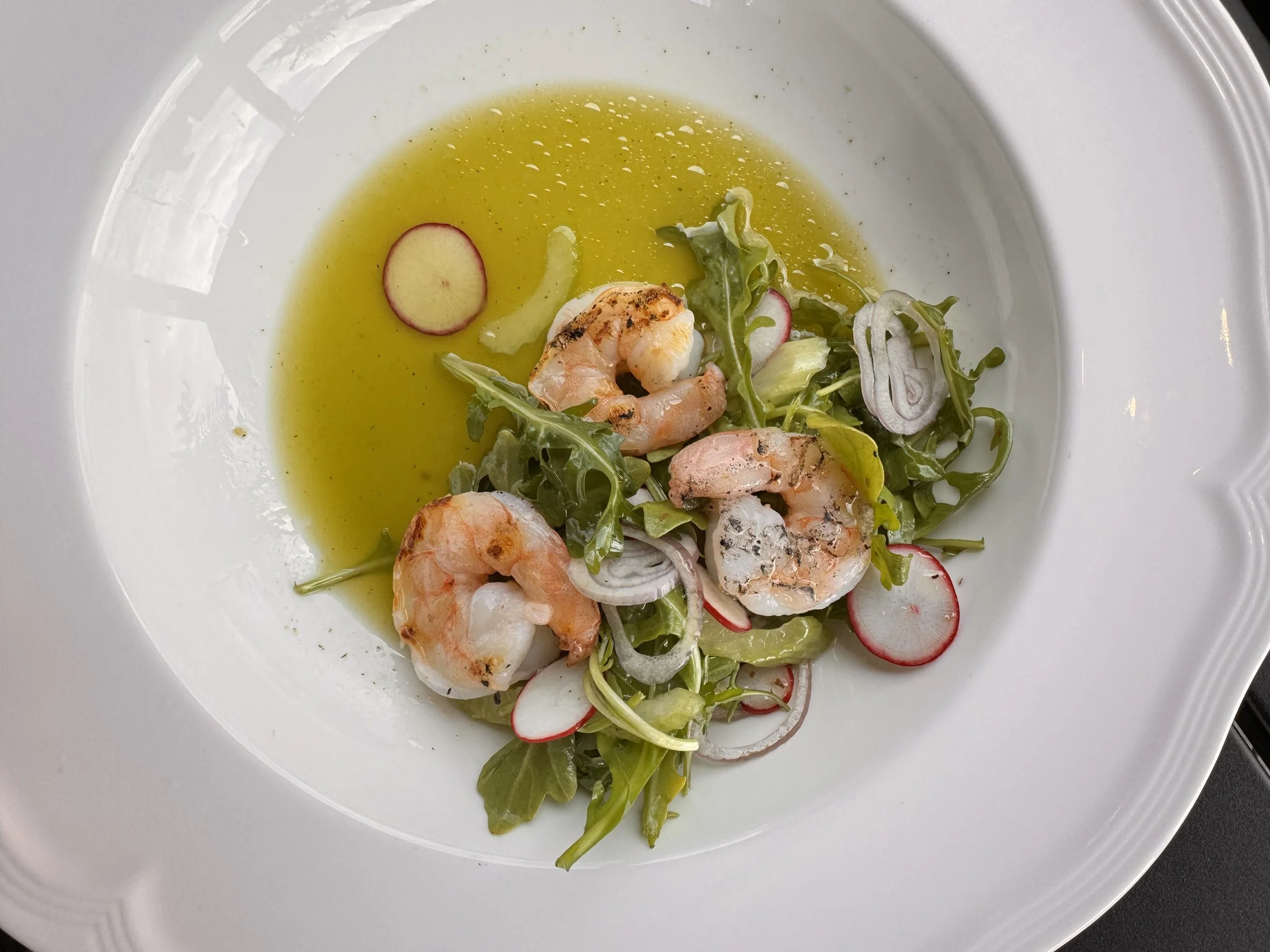 Salad with grilled shrimp, radish slices, and onions in a yellow vinaigrette on a white plate