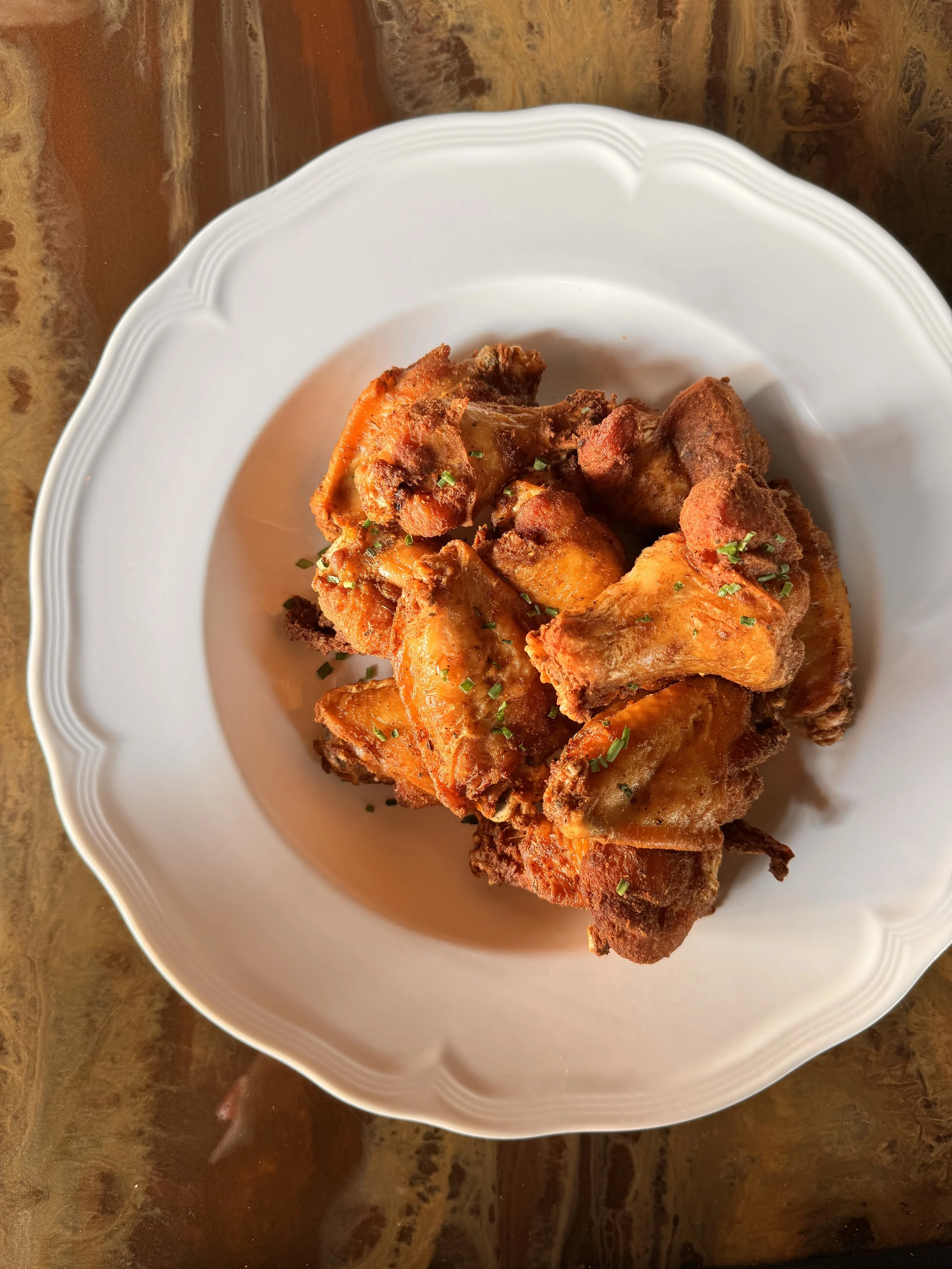Fried chicken wings garnished with chopped herbs on a white decorative plate.