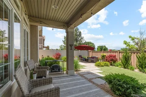 Covered patio with wicker chairs, outdoor furniture, a red umbrella, and a landscaped backyard with trees and shrubs.