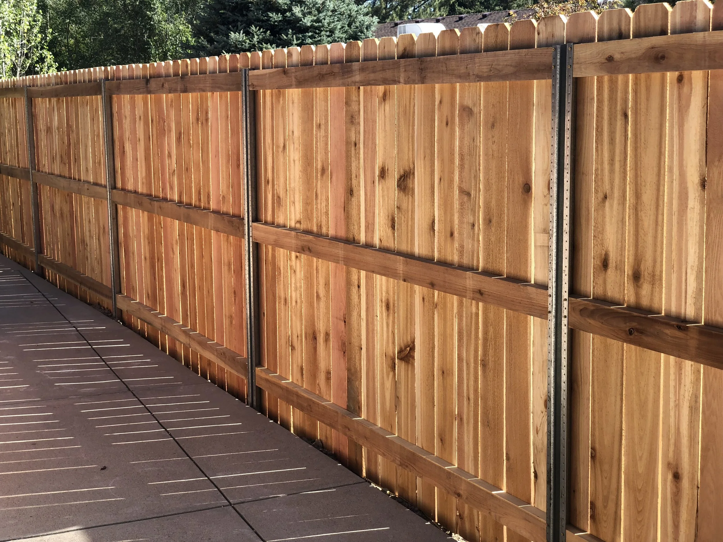 New wooden privacy fence installed along a sidewalk, casting shadows on the concrete ground.