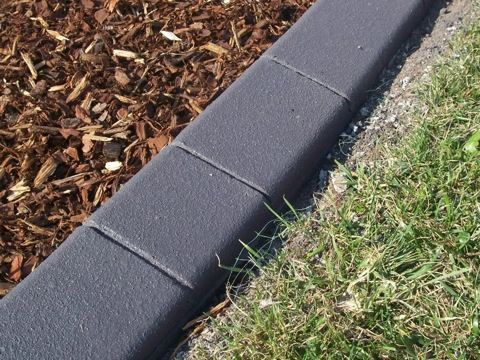 Close-up of a black plastic edging bordering a garden bed with mulch on one side and grass on the other.