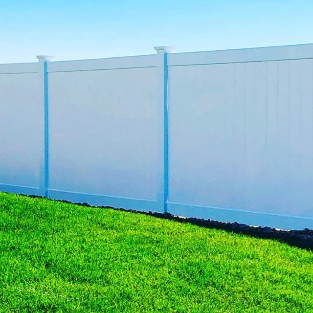 A white privacy fence next to a green lawn under a clear blue sky.