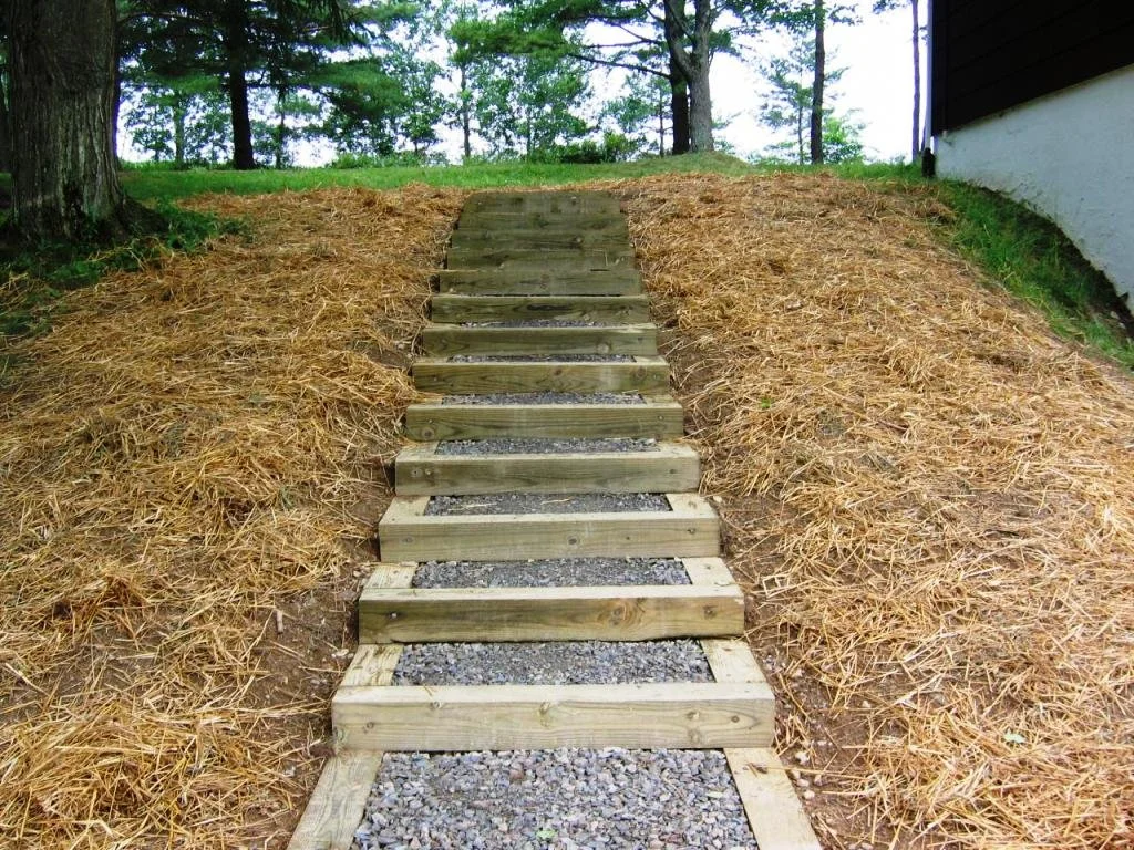 Wooden stairs leading up a small hill, surrounded by straw-covered ground and trees in the background.