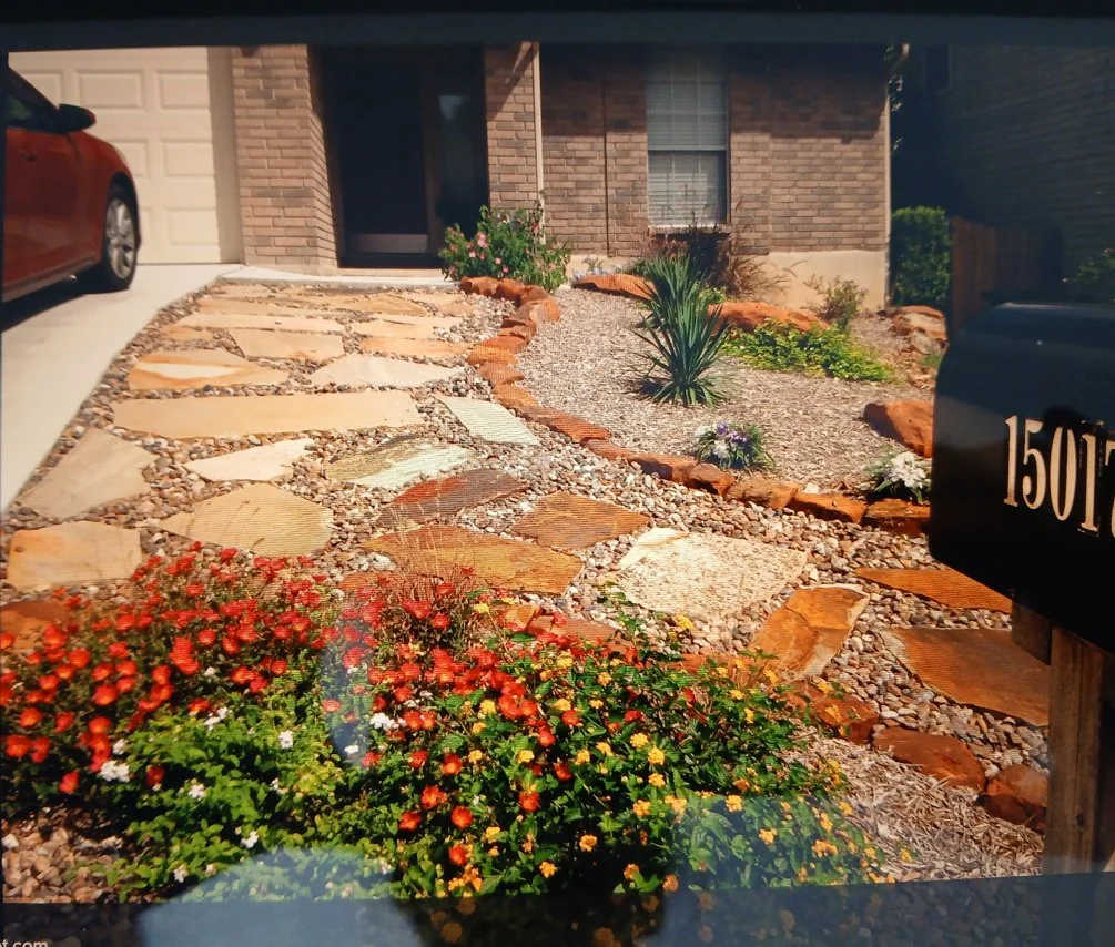 A front yard with a stone and gravel pathway leading to a house entrance, surrounded by desert-style landscaping with drought-tolerant plants, bushes, and colorful flowers. A black mailbox with the number 1507 is visible on the right.