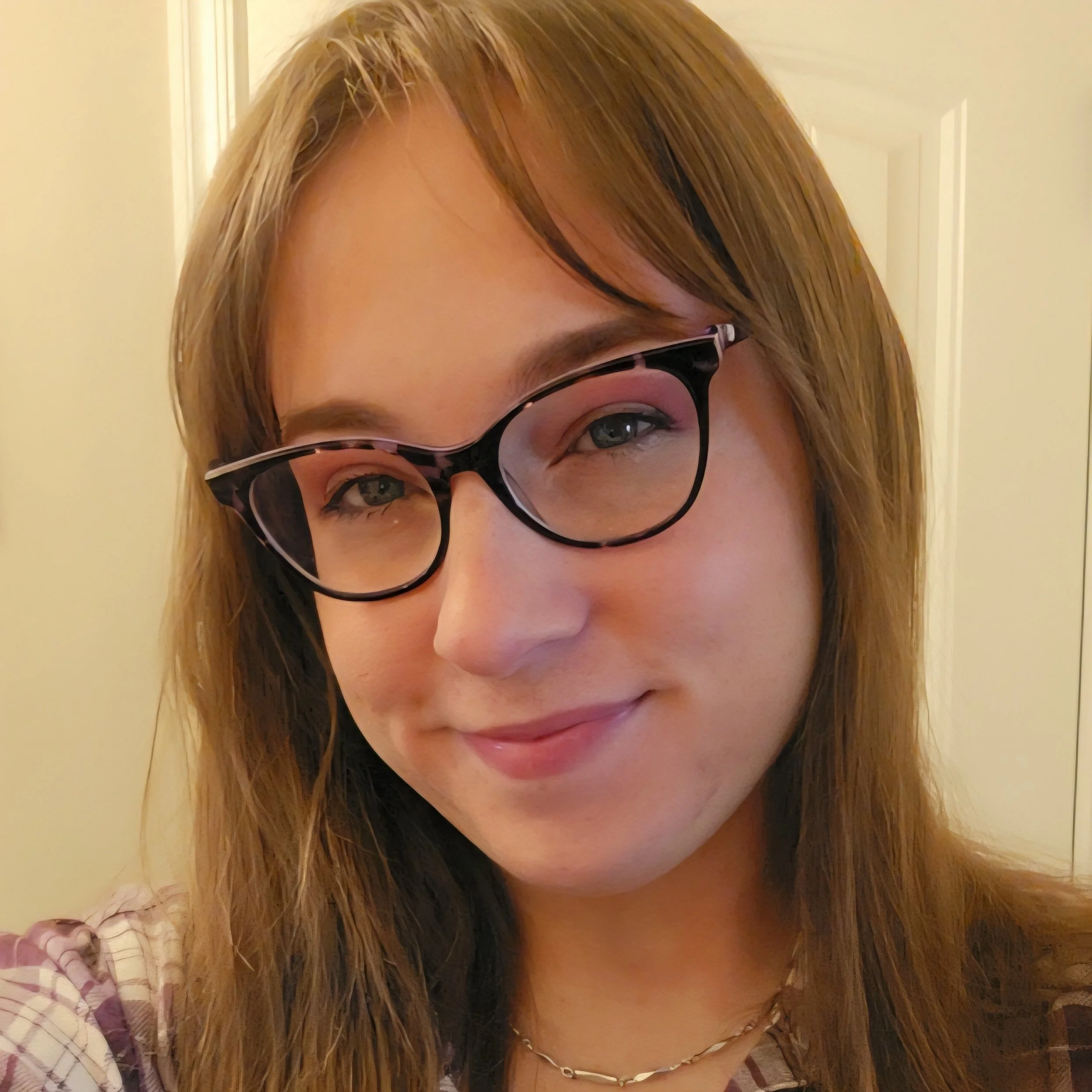 A woman with long, wavy, light brown hair, wearing glasses with black frames, and a shell necklace. She is tilting her head and smiling slightly, with a door in the background.