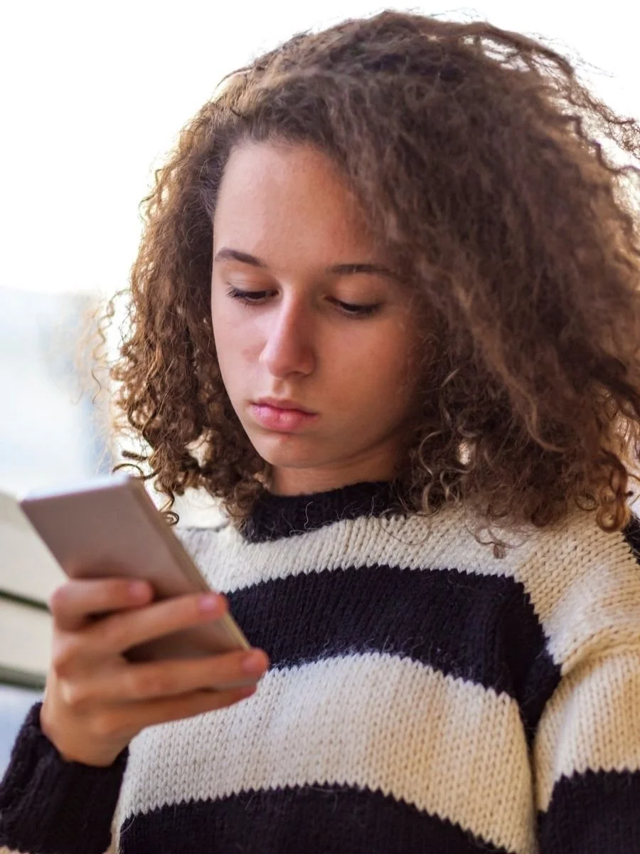 Teenager looking at her phone, seemingly unhappy