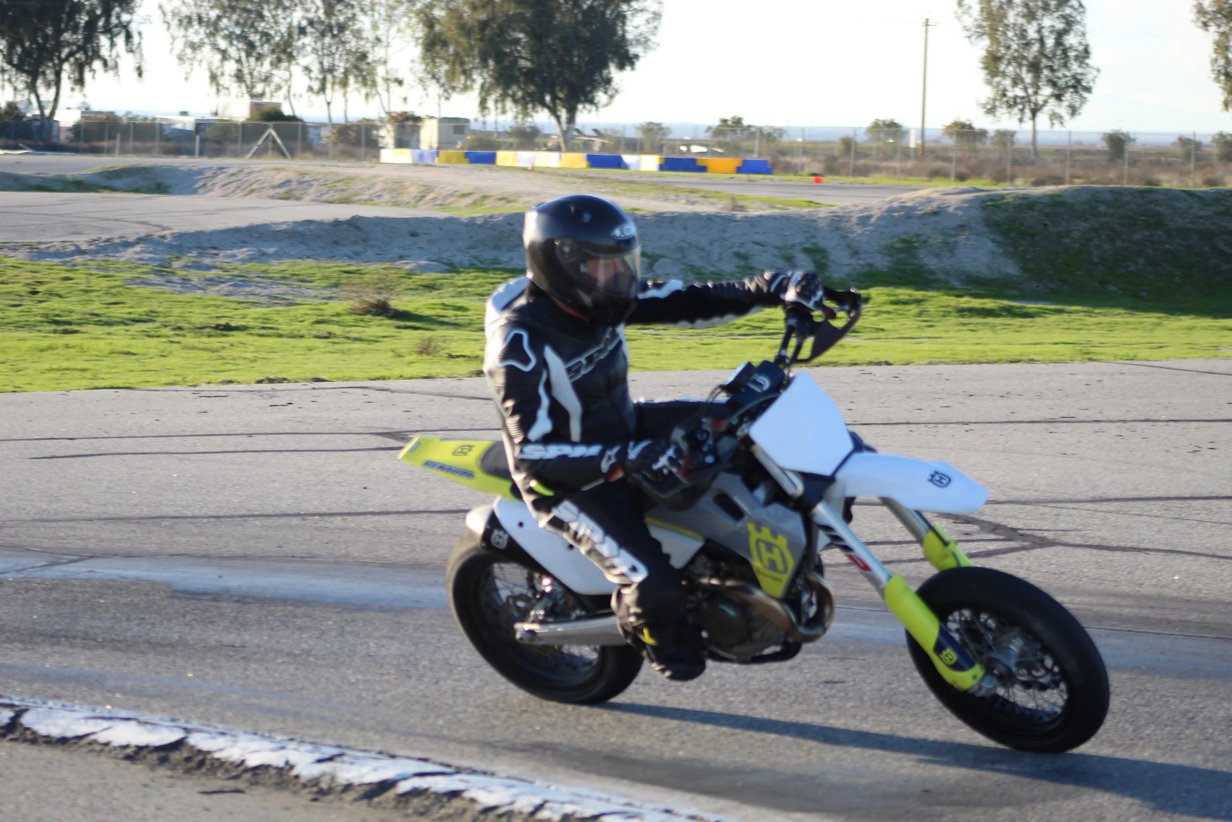 Motorcycle rider in a black helmet and black riding gear on a yellow and white dirt bike, racing on an outdoor track.