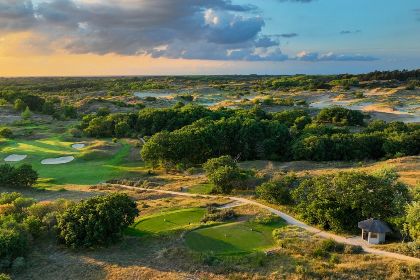 A long expanse of golf course can be seen with sun adding a yellow hue between the shadows.