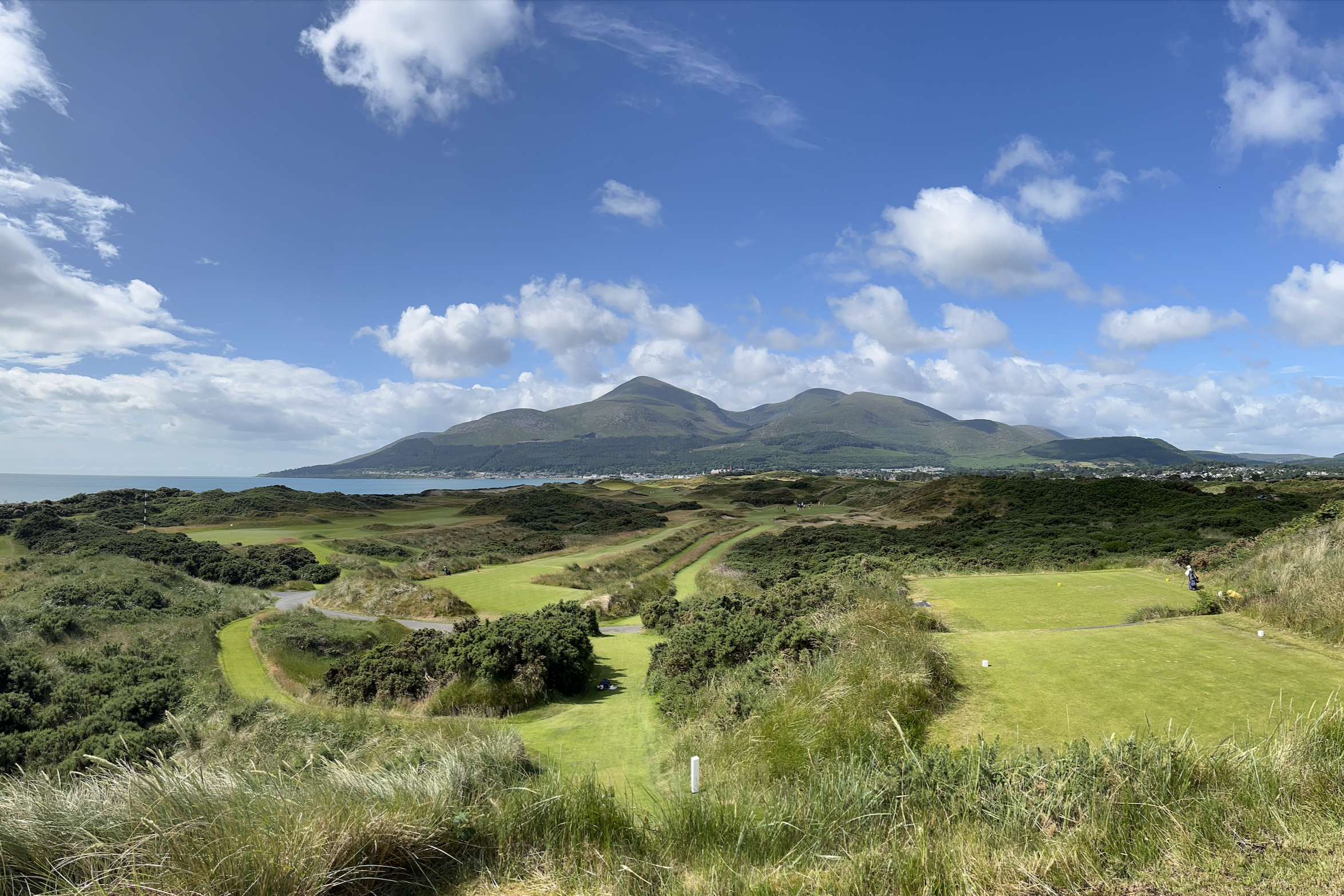An elevated view of Royal Dornoch golf course, with the golf course in the foreground and ocean and mountain views behind.