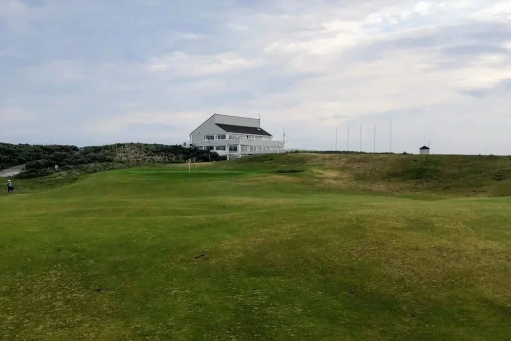 A white clubhouse stands high above a golf course.