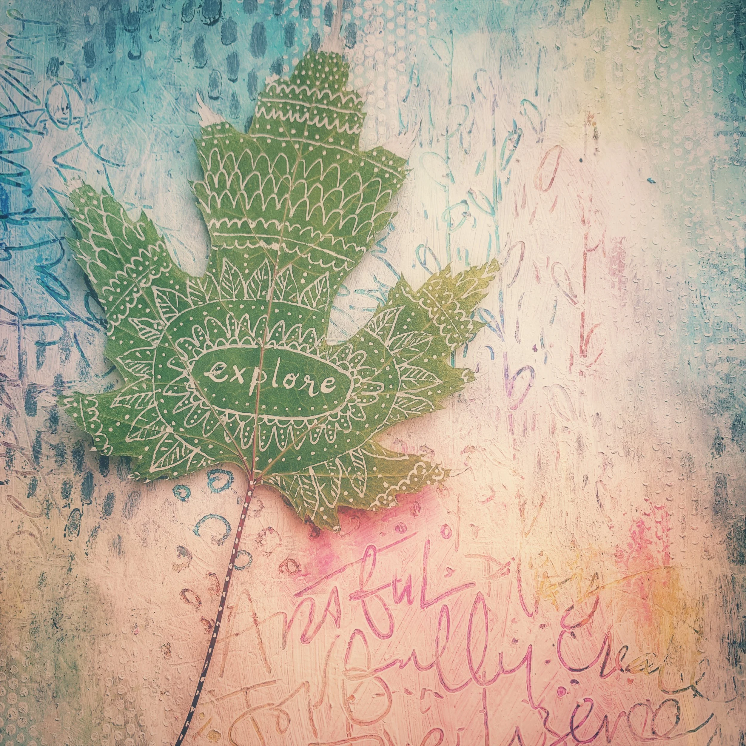 A paper leaf with intricate white doodles and the word "explore" written in the center, set against a textured colorful background with faint handwritten words.