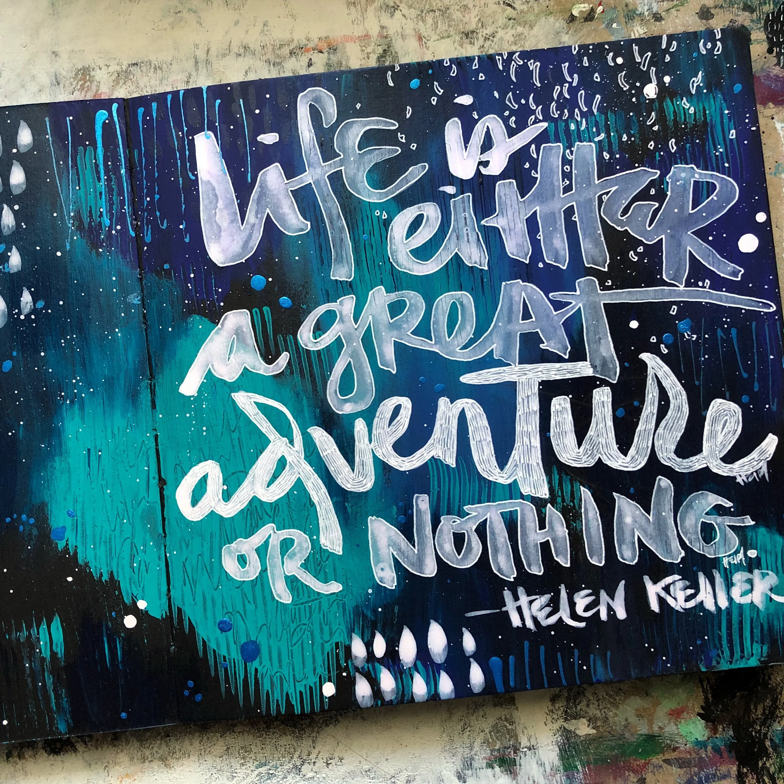A watercolor painting with a quote by Helen Keller that reads, 'Life is either a great adventure or nothing' - Helen Keller.' The background features shades of blue, teal, and purple with abstract splashes and brushstrokes.