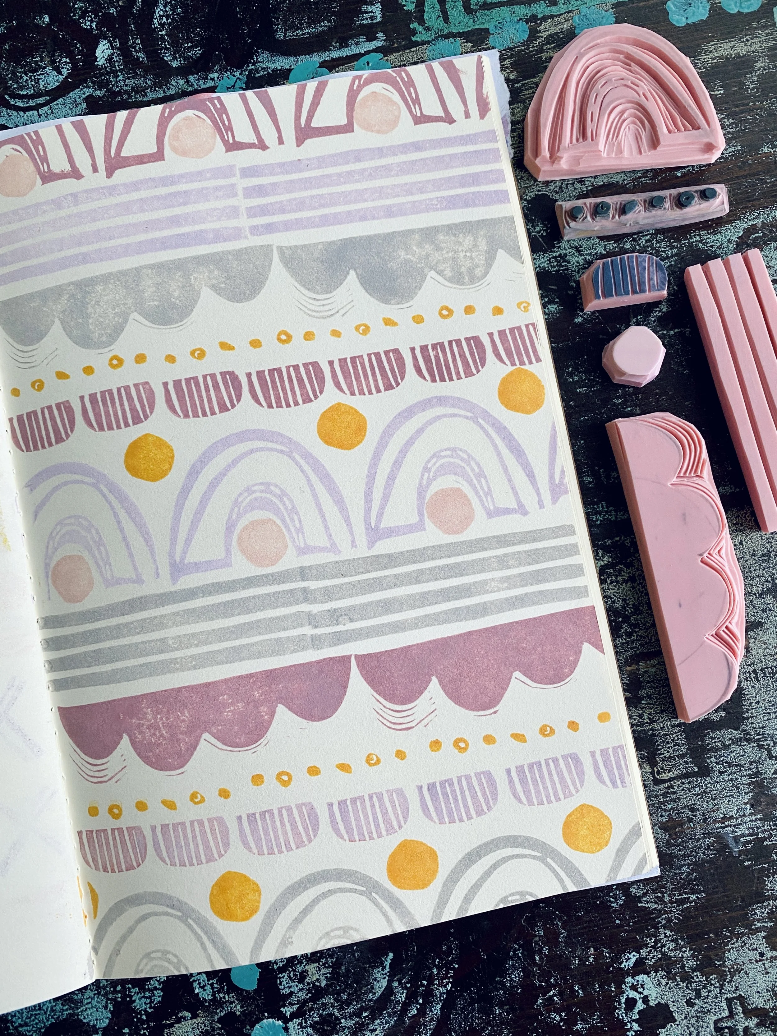 A notebook with pastel-colored abstract patterns, surrounded by pink erasers and pastel-colored eraser caps on a dark textured surface.