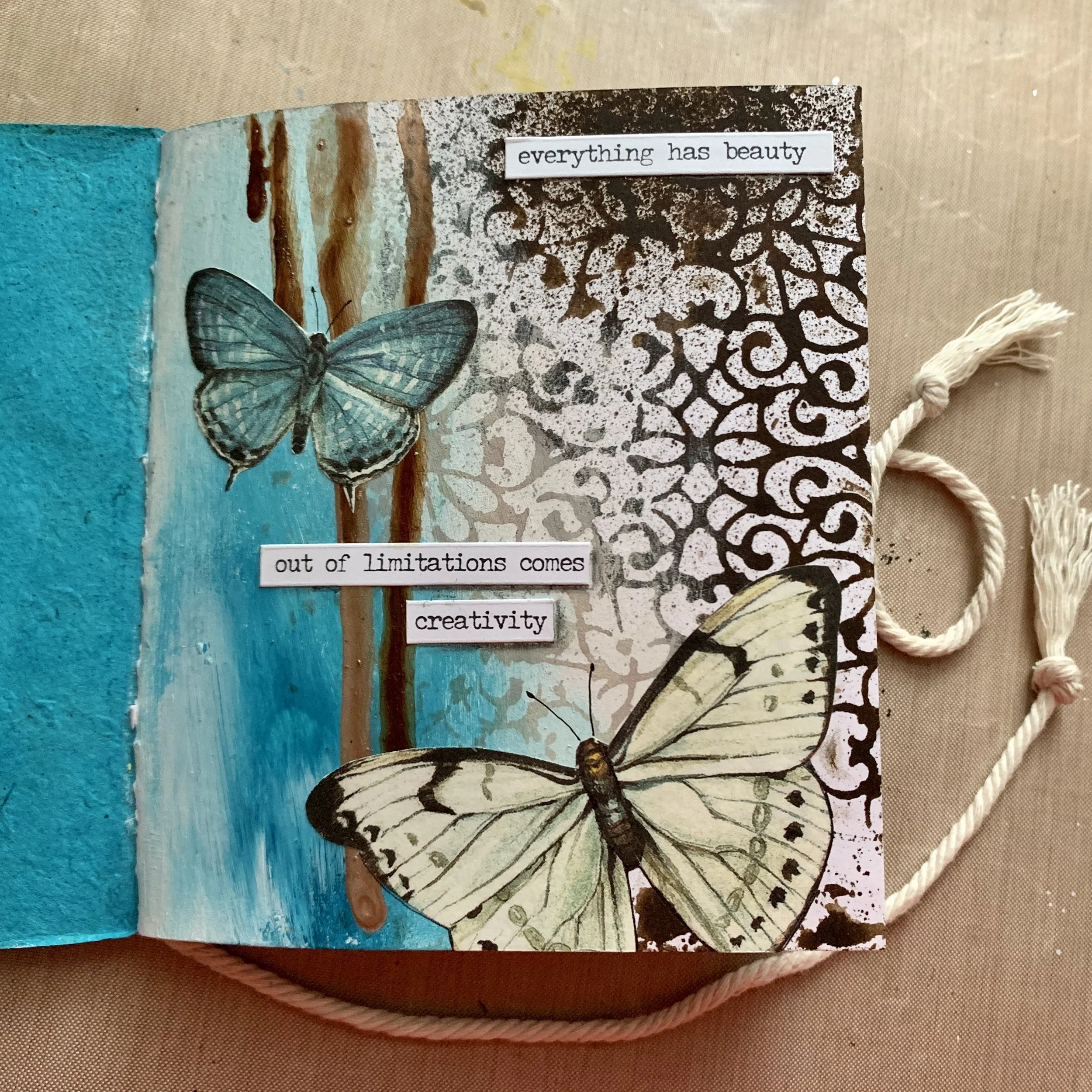 An open handmade sketchbook featuring painted blue and black butterflies and inspirational text that reads, "everything has beauty out of limitations comes creativity," with a decorative black and white patterned background and a blue textured page o