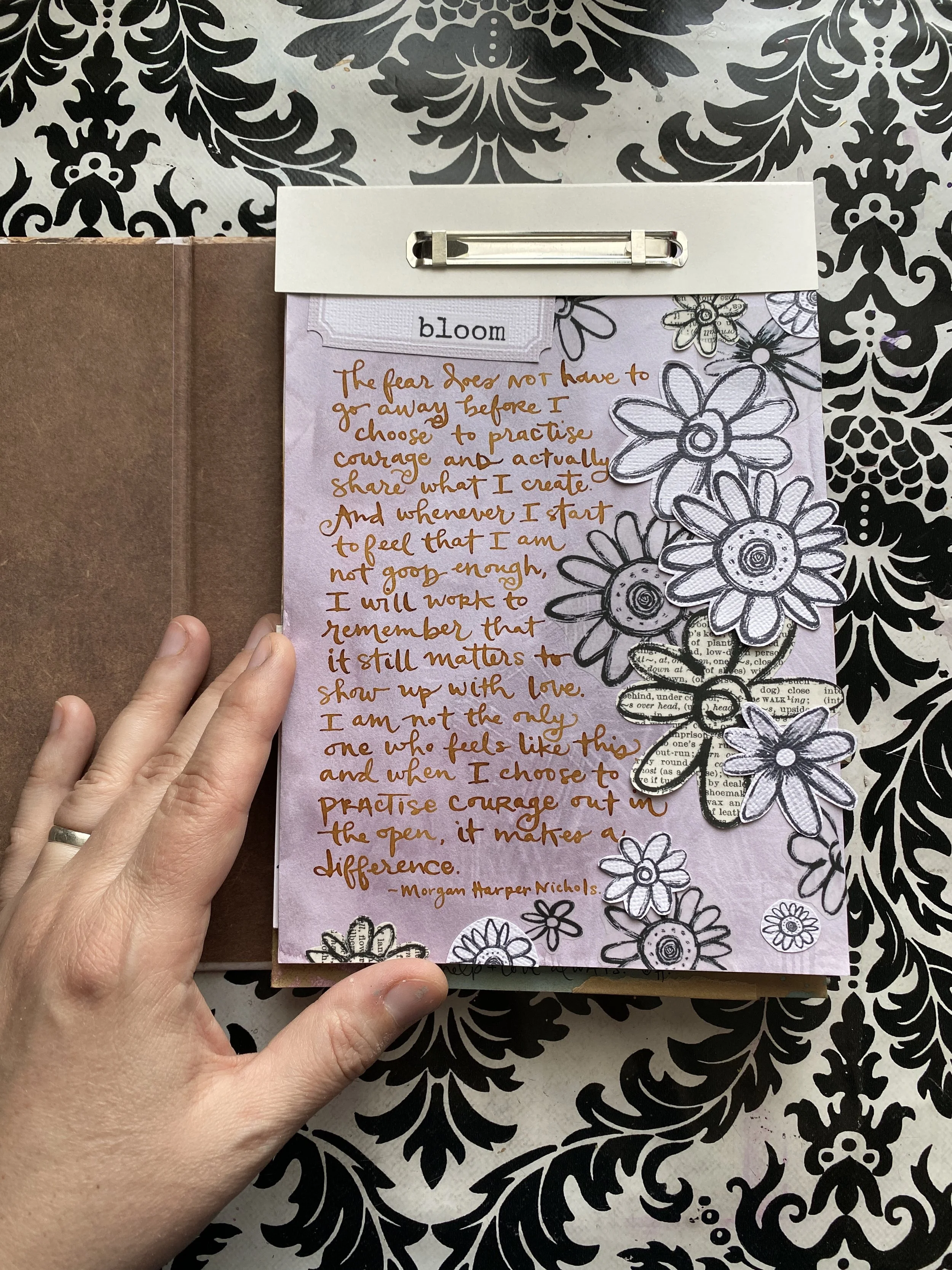 A handwritten note with a quote on pink paper, decorated with black and white flower illustrations, held over a black and white patterned background.