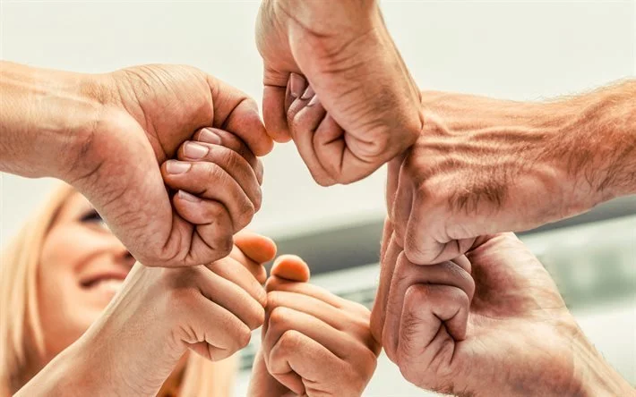 Grupo de personas juntando puños en señal de unión y cooperación.