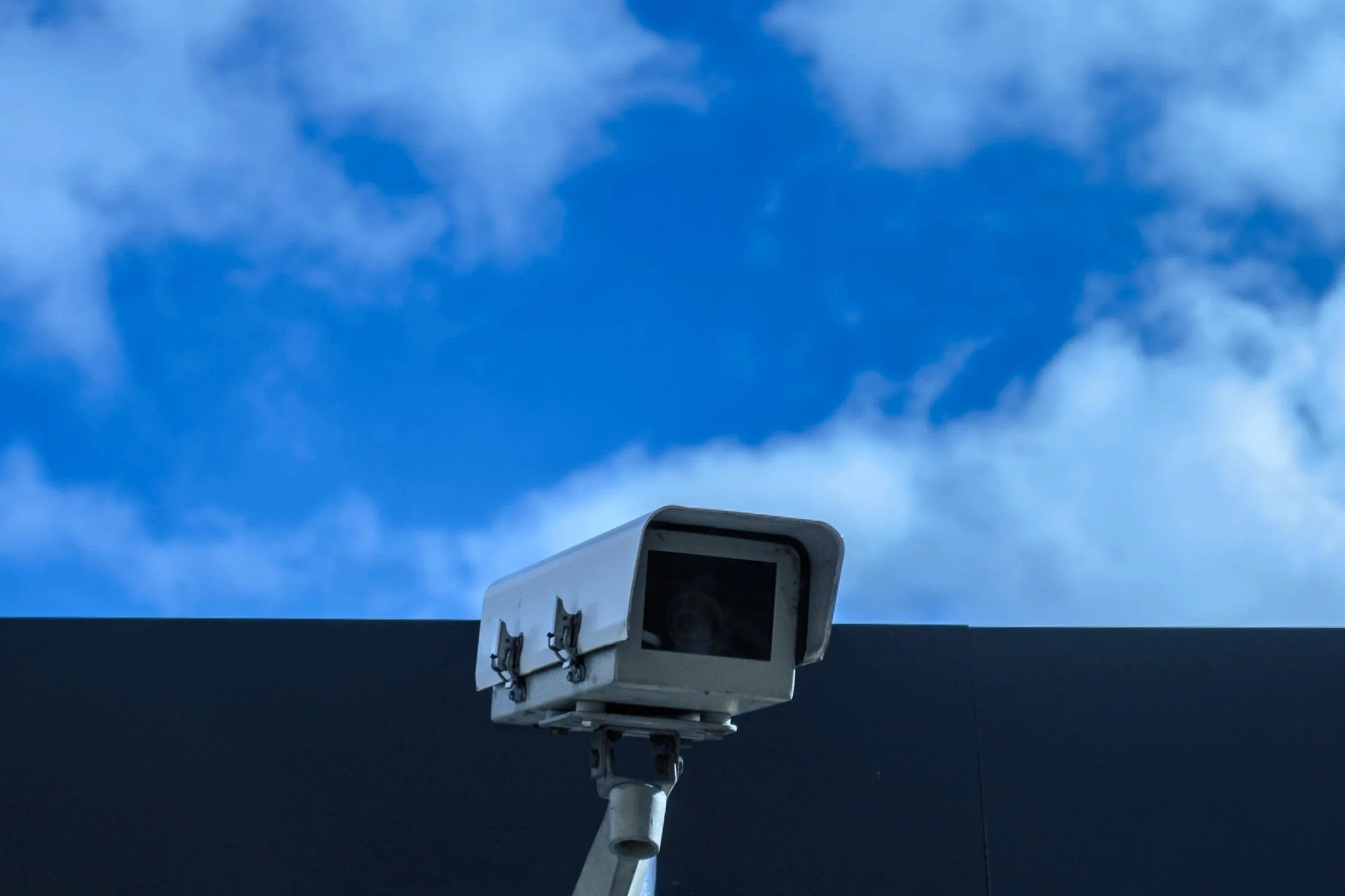 Security camera mounted on a building against a blue sky with clouds.