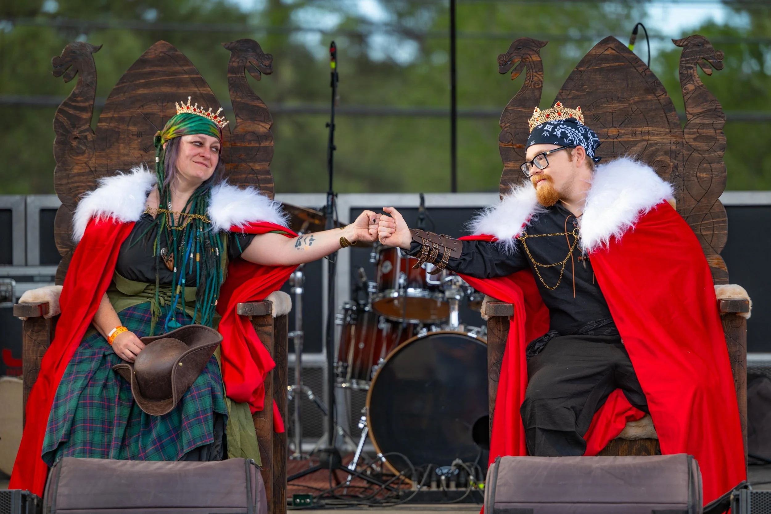 2025 Lincoln Forest Ren Faire's crowned King and Queen sit on their thrones onstage and bump fists in celebration.