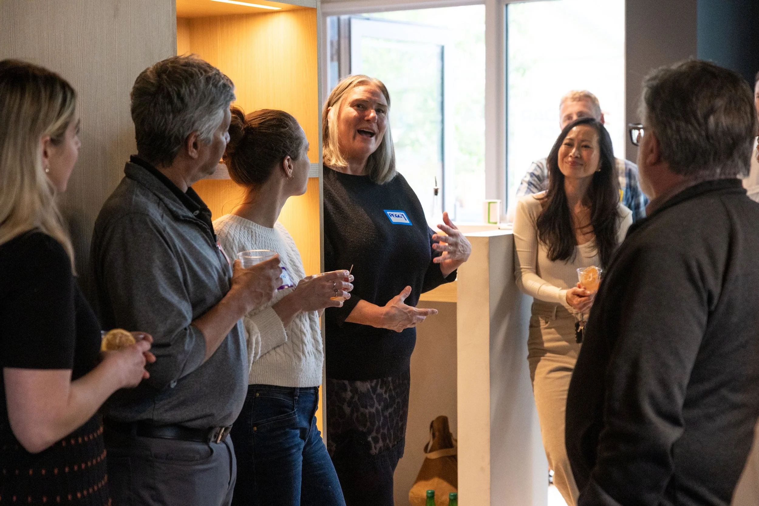 Group of seven people engaged in conversation at an indoor gathering, with some holding drinks.