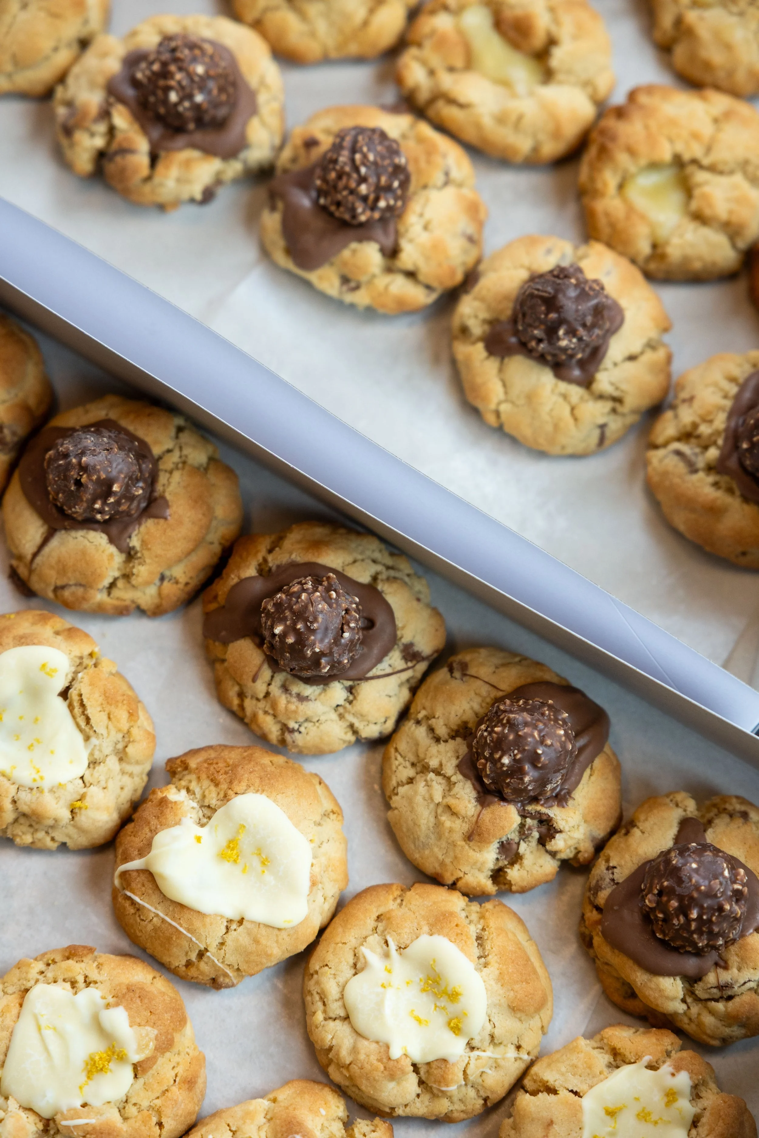 Assorted cookies on baking sheet, including chocolate-dipped cookies topped with a truffle, and white frosted cookies with lemon zest.