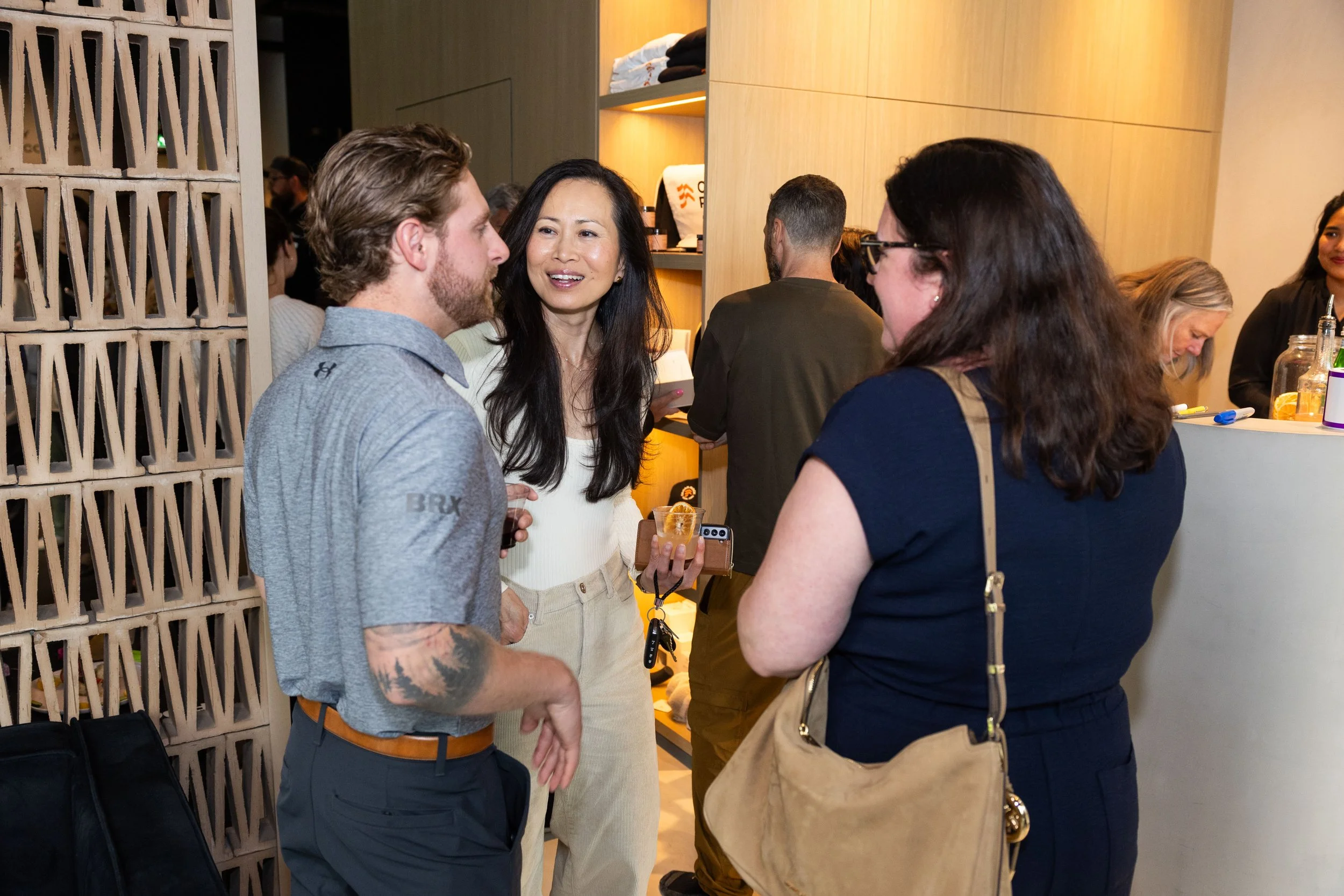 People talking in a social setting, a man with a beard and a woman holding a drink are engaged in conversation, with other guests visible in the background.