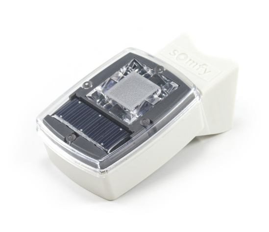 A white rectangular solar-powered sensor or device with a transparent top revealing a solar panel and components inside, branded with "Somfy."