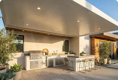 Covered outdoor kitchen with grill, sink, and bar stools.