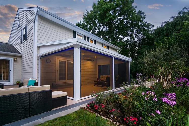 Modern house with screened patio, outdoor seating area, and colorful garden in twilight.