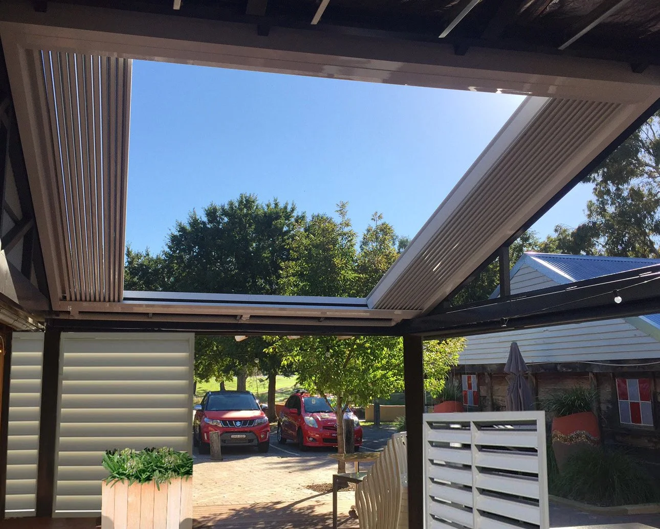 Outdoor patio with open louvered roof and trees in background
