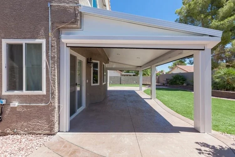 Covered patio with sliding glass doors, beige textured walls, and a small yard with artificial grass and trees.