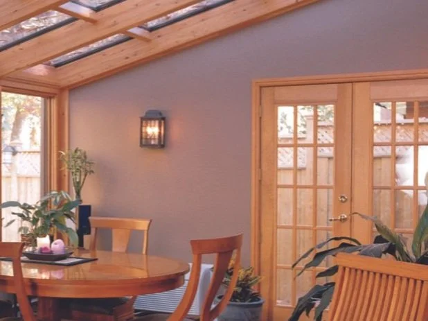 Sunroom with wooden furniture, round table, skylight ceiling, plants, and French doors.