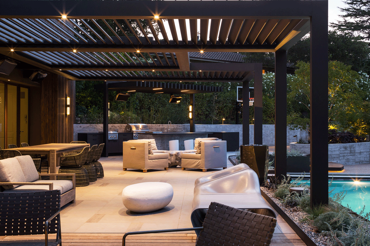 Modern outdoor patio with seating area, lounge chairs, dining table, and a small swimming pool, illuminated by string lights and surrounded by trees.