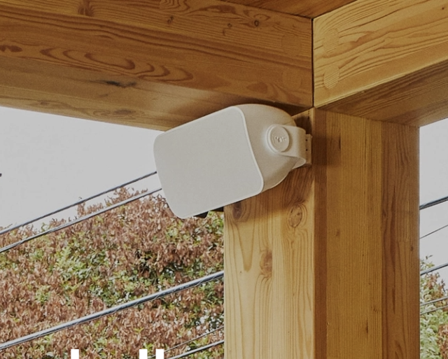 Outdoor white speaker mounted on a wooden beam.
