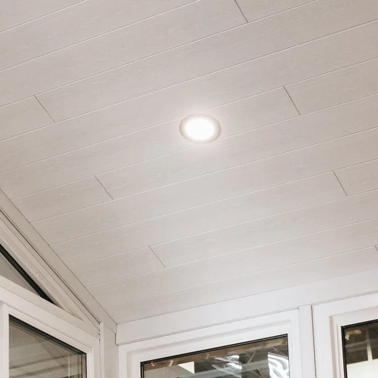 White paneled ceiling with a recessed light and part of a window frame.