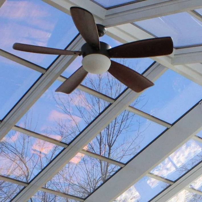 Ceiling fan under glass roof with blue sky and tree reflection