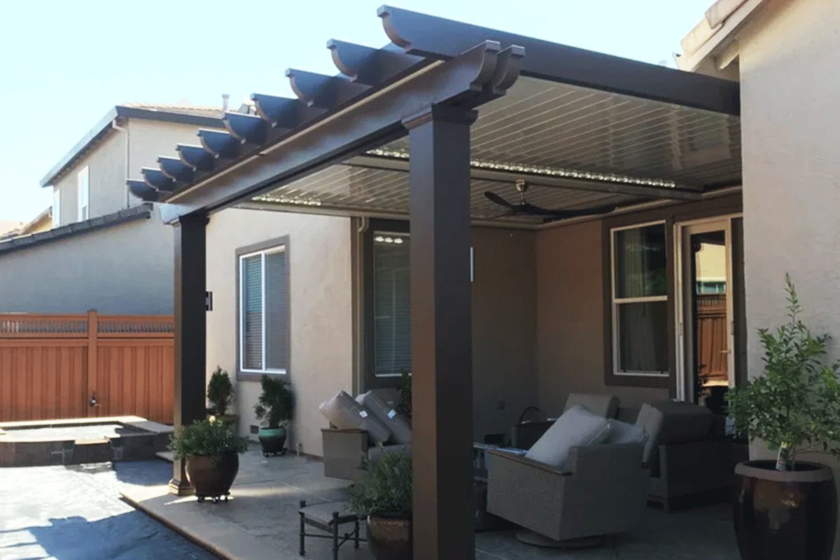 Back patio of a house with a covered seating area, outdoor furniture, potted plants, and a wooden fence in the background.