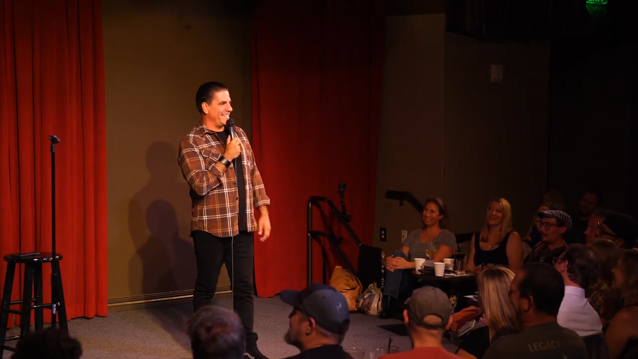 Comedian performing stand-up comedy on stage in front of an audience.