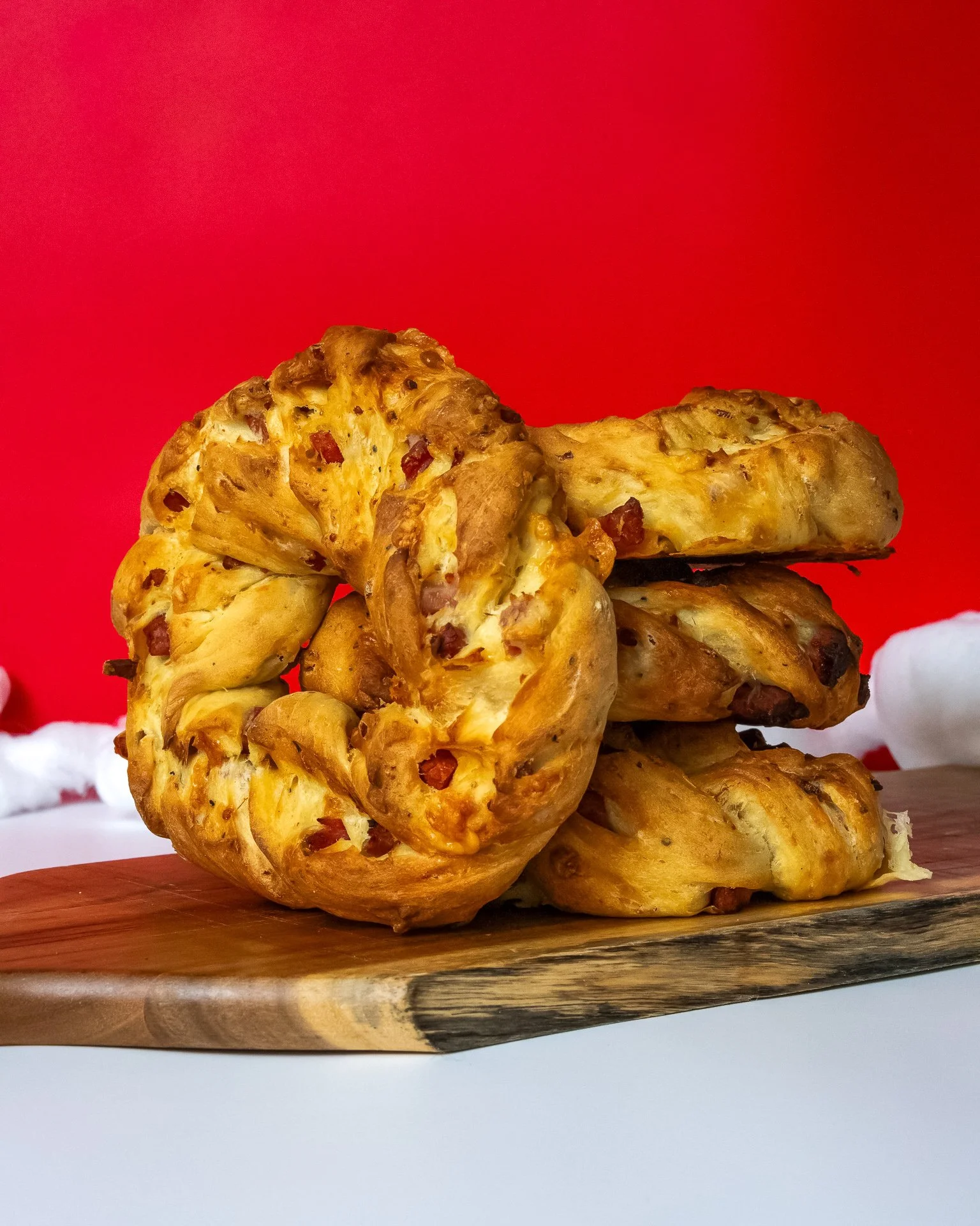 Stack of cheesy, baked bread with bits of bacon on a wooden board, against a red background.