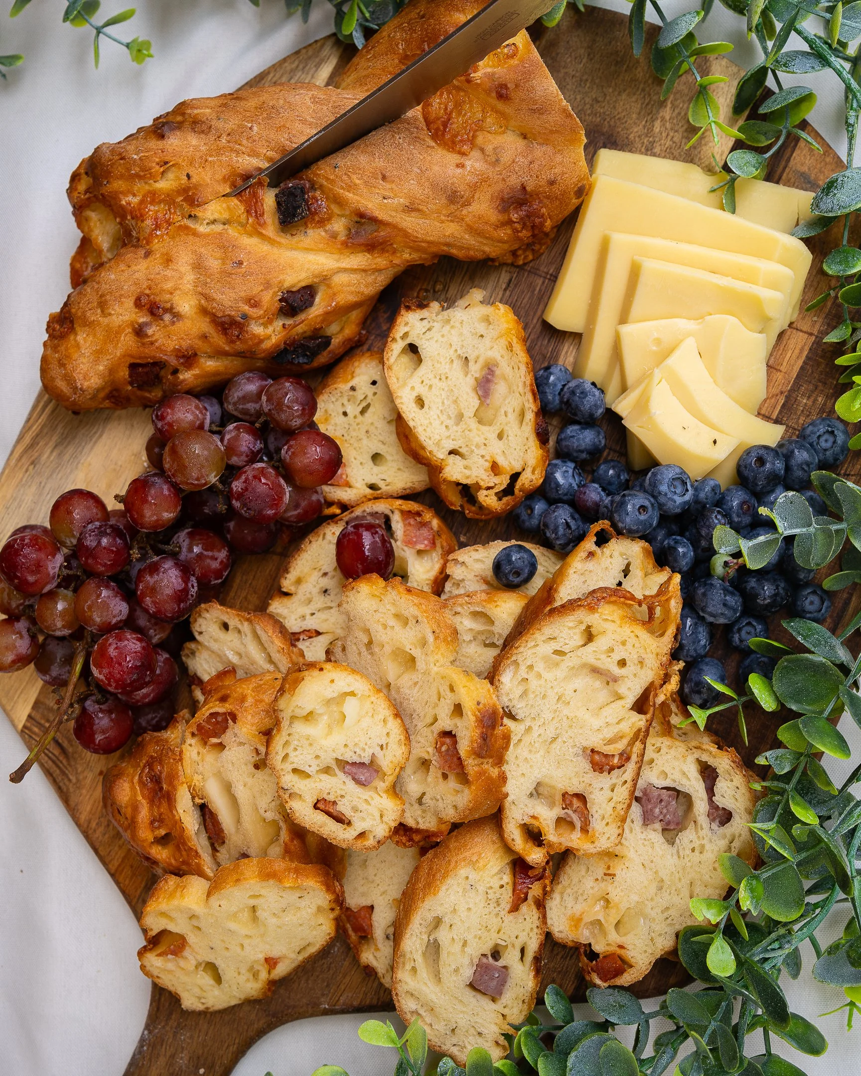 A cheese and bread board with grapes and blueberries on a wooden serving board.