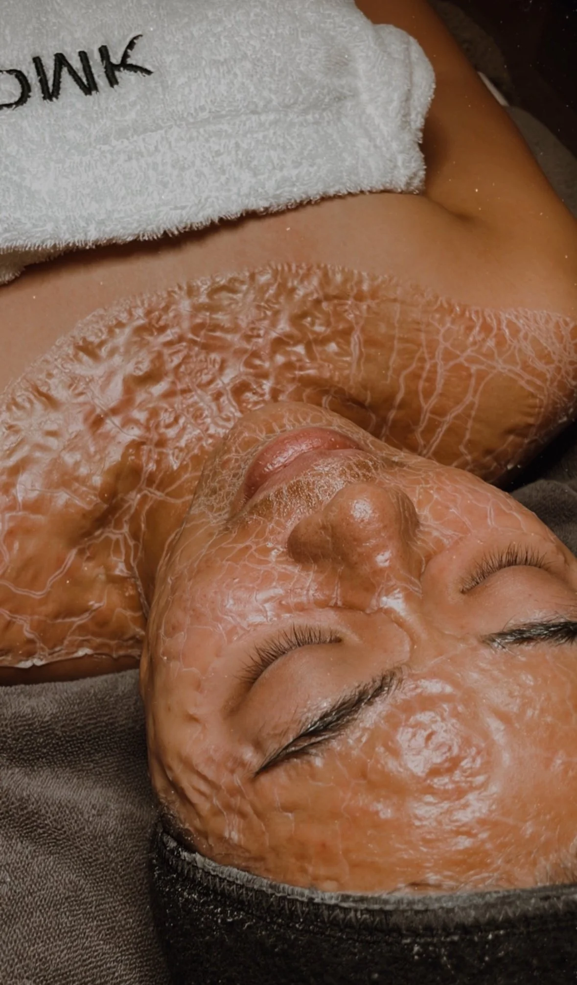 Person receiving DMK enzyme treatment with a towel wrap on in a spa setting.