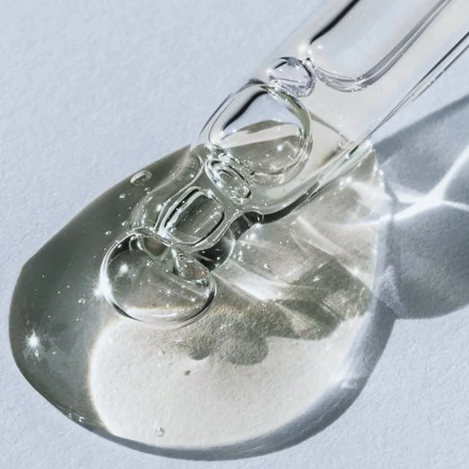 Close-up of a clear liquid dropper with a drop of liquid on a reflective surface.