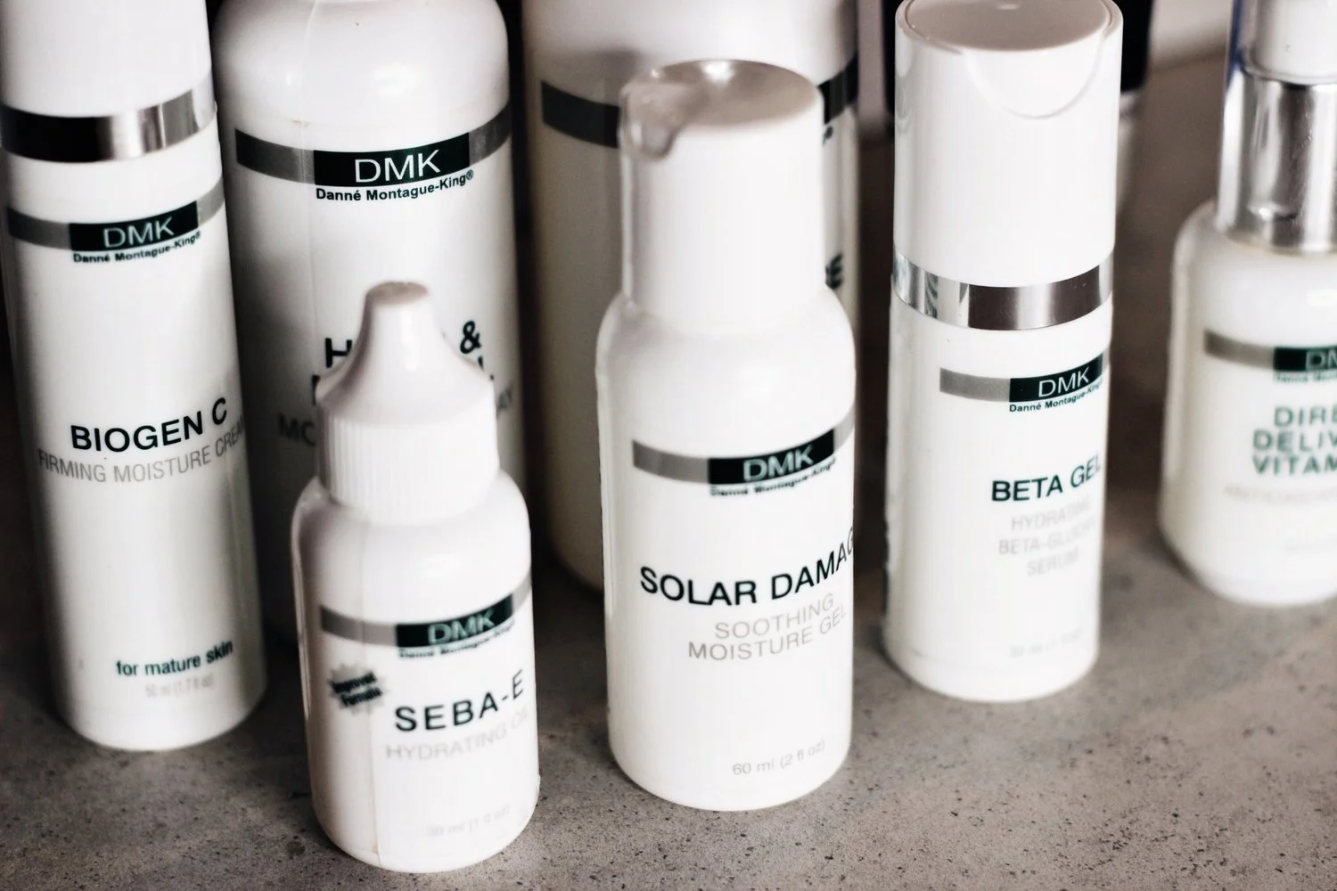 Various DMK skincare product bottles including Biogen C cream, Solar Damage Gel, and Beta Gel Serum on a countertop.