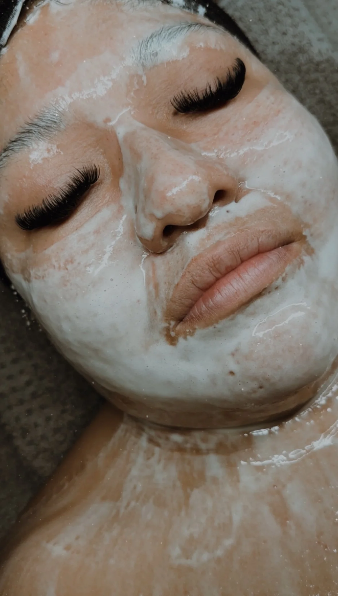 Close-up of a person's face with DMK enzyme face mask applied, eyes closed, and with lashes.