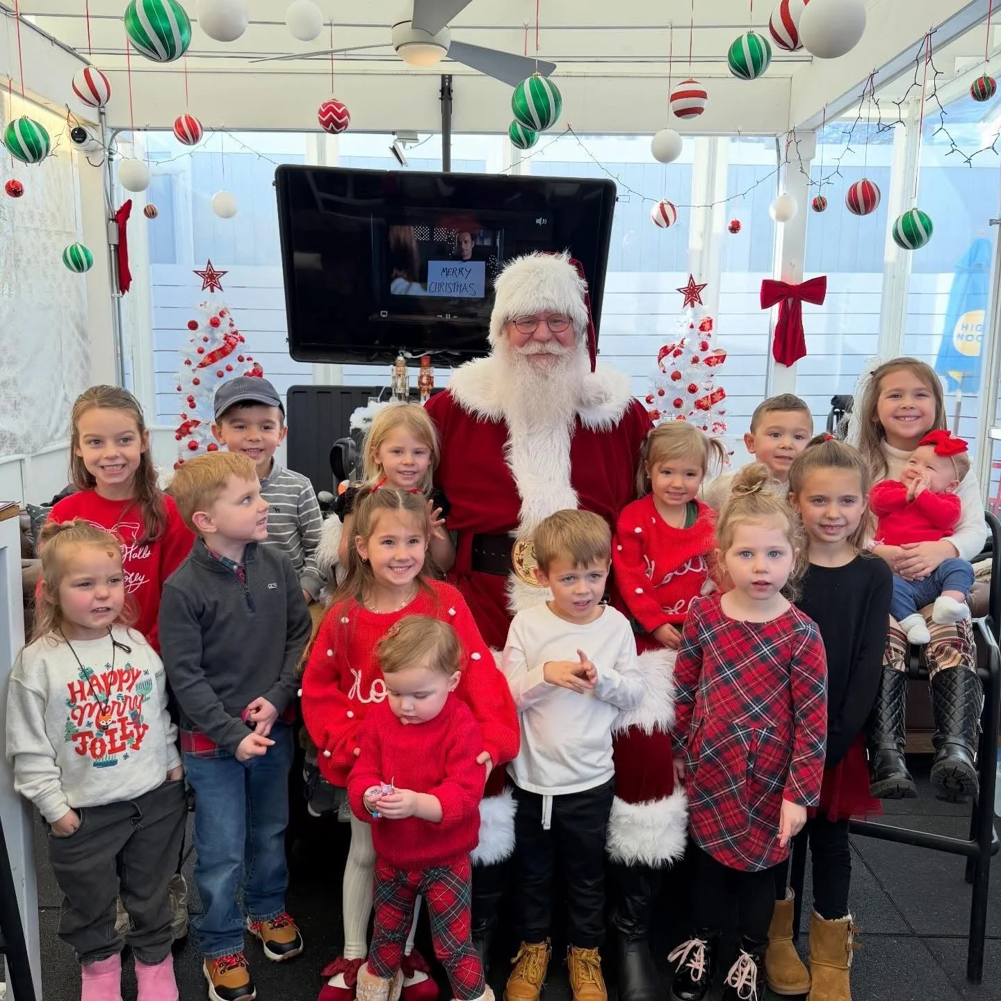 Group of children and Santa Claus posing for a photograph in a decorated festive setting with Christmas trees and ornaments.