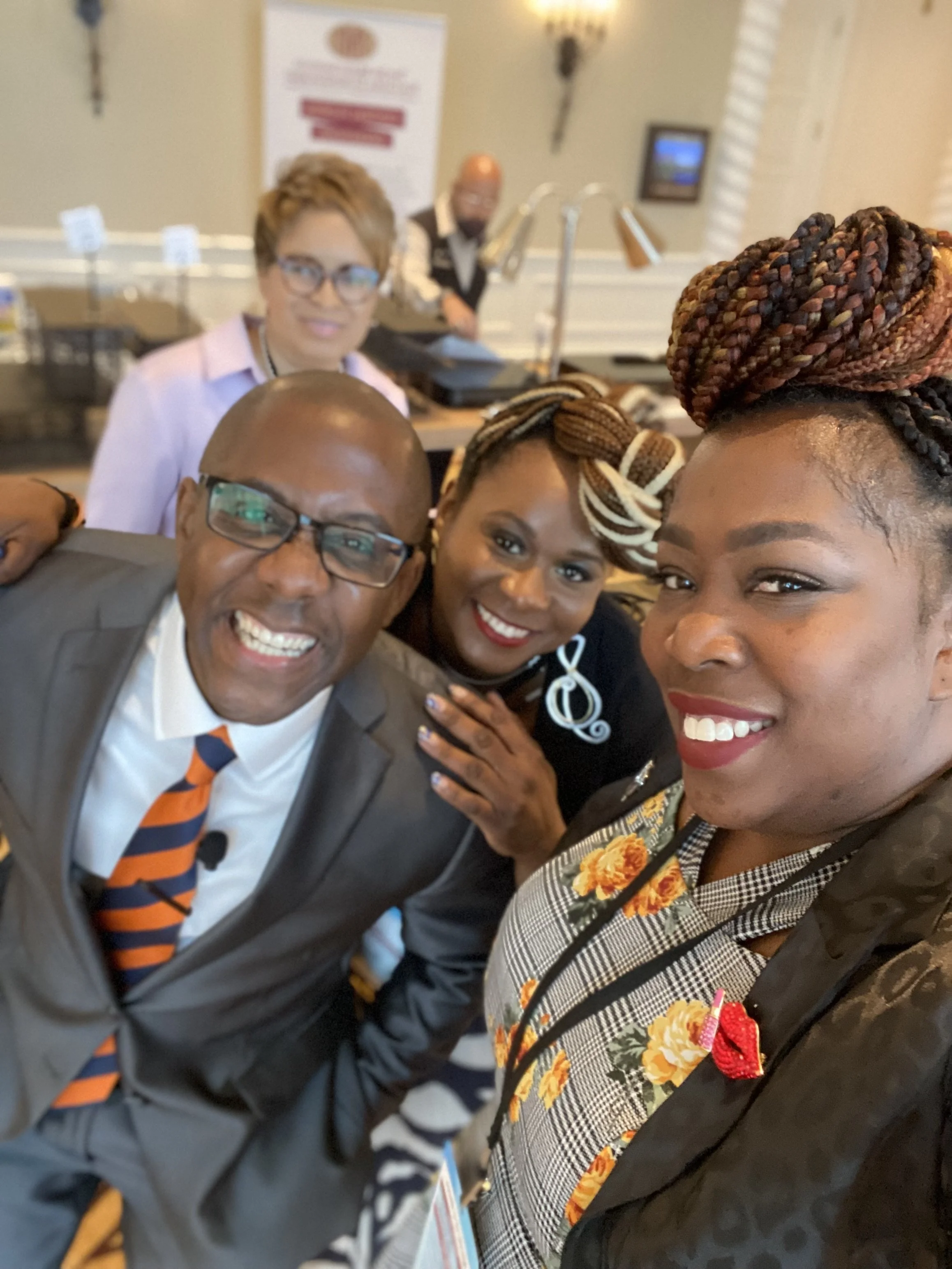 Group of five diverse adults smiling for a selfie at an indoor event.