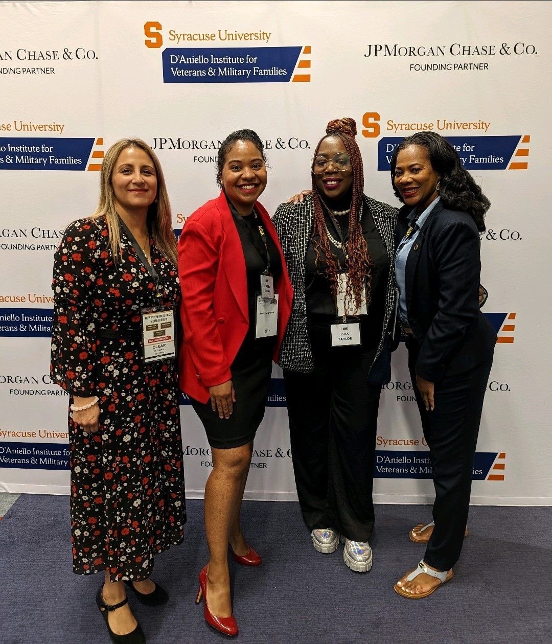 Four women standing together at an event, smiling, in front of a backdrop with the logos of Syracuse University, JPMorgan Chase & Co., and the D'Aniello Institute for Veterans & Military Families.